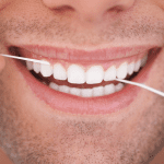 man with a white smile and stubble flossing between his teeth
