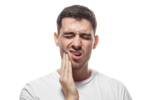 man against a white background holding his jaw, severe tooth pain, possible need for a root canal