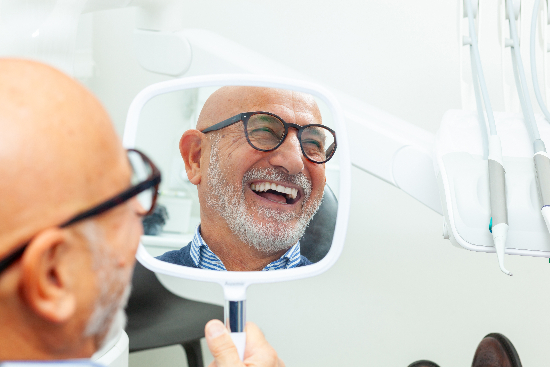 older man smiling at his new dental implants in a handheld mirror