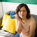 young woman sitting on a couch with an ice pack, serious tooth pain