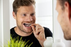 male adult placing his clear aligners while looking into mirror